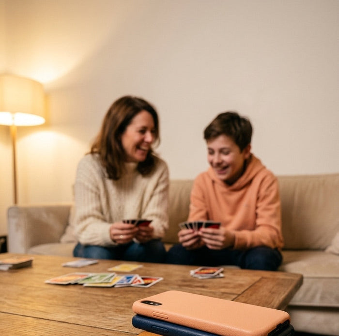 Une mère et son fils jouent aux cartes sur le canapé, leurs téléphones empilés sur la table basse