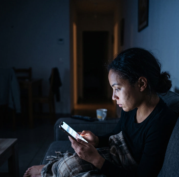 Une femme seule sur son canapé, tard le soir, le visage éclairé par son téléphone
